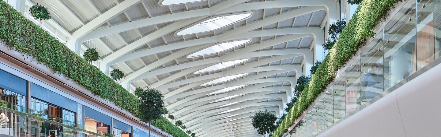 Atrium of a shopping mall featuring lush plants growing from the ceiling, creating a vibrant and inviting atmosphere.