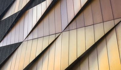 Nahaufnahme einer modernen Gebäudefassade mit geometrischen Metallpaneelen in Gold- und Bronzetönen.