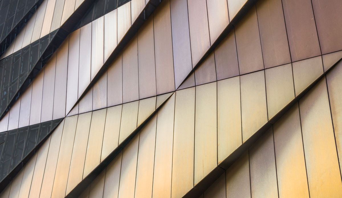 Nahaufnahme einer modernen Gebäudefassade mit geometrischen Metallpaneelen in Gold- und Bronzetönen.