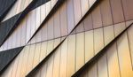 Nahaufnahme einer modernen Gebäudefassade mit geometrischen Metallpaneelen in Gold- und Bronzetönen.