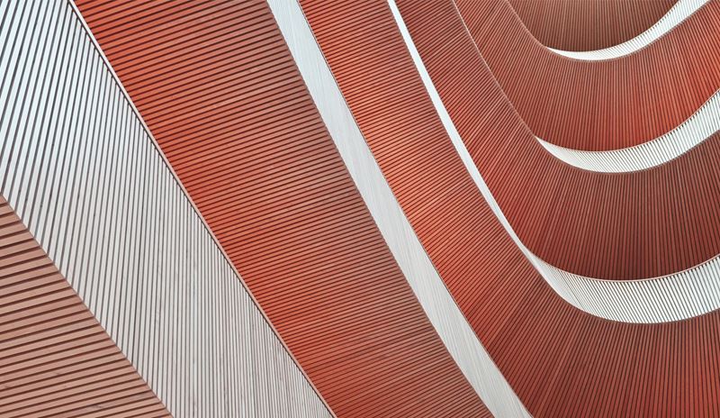 Abstraktes architektonisches Detail mit geschwungenen terrakottafarbenen Oberflächen mit geometrischen Linienmustern und weißen Strukturelementen