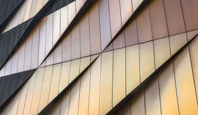Nahaufnahme einer modernen Gebäudefassade mit geometrischen Metallpaneelen in Gold- und Bronzetönen.