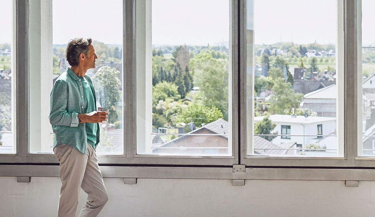 A man stands by a window, gazing thoughtfully outside into the distance.