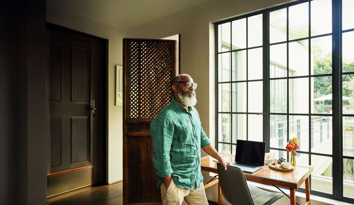 Person standing beside a desk near large sunlit windows