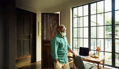 Person standing beside a desk near large sunlit windows