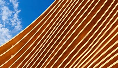 A modern building facade with diagonal white stripes over a reddish-brown surface