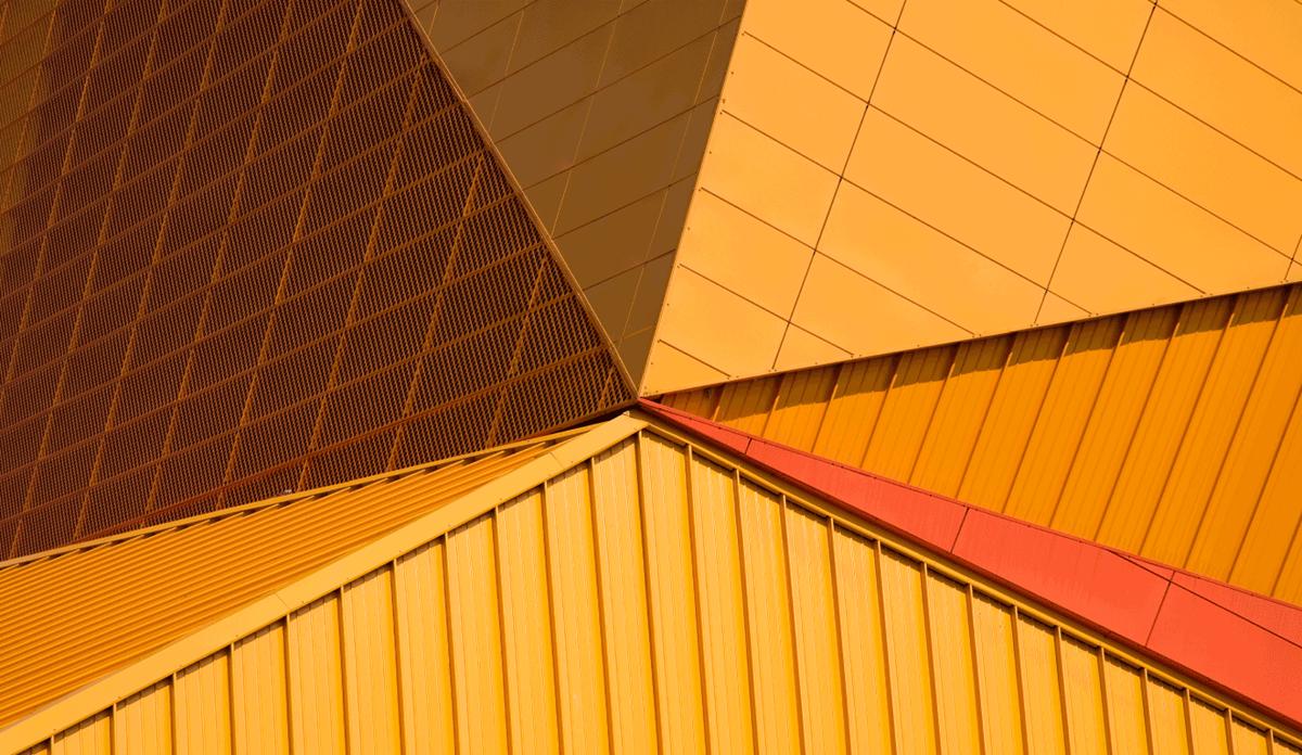 Abstract close-up of angular modern building facade in warm gold, orange, and red tones