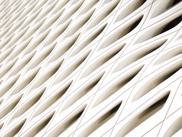 Close-up view of a modern white architectural facade with a repeating pattern of curved, eye-shaped openings arranged in diagonal row.