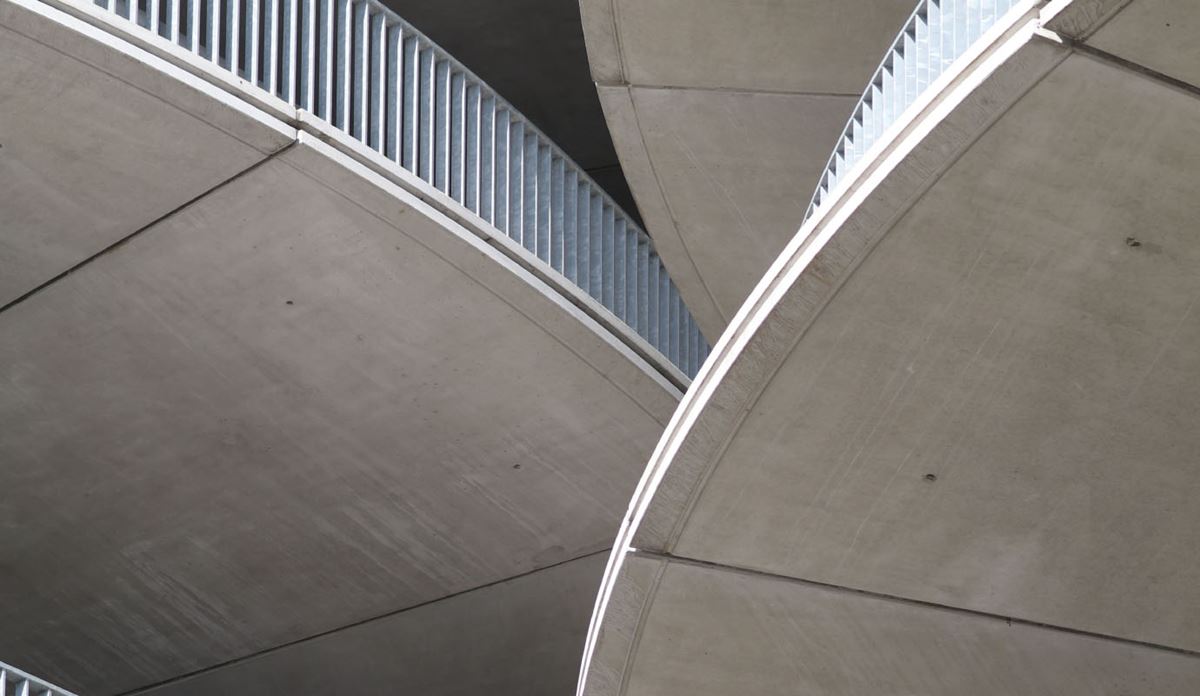 Curved concrete architectural structure with a triangular opening and vertical metal railings, viewed from below.