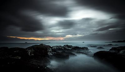 Dark rocky seashore under cloudy sky.