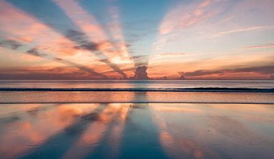 Sunset over a clam ocean with dramatic sun rays reflecting on wet send.