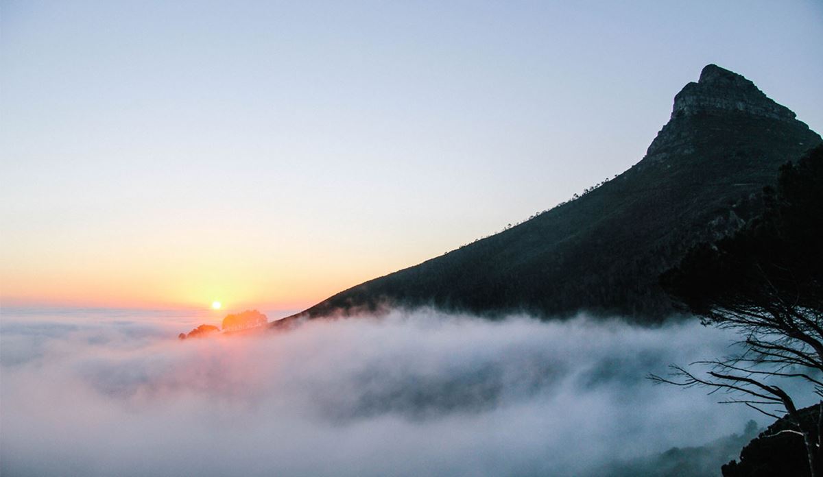 Pyramid-shaped mountain peak rising above fog at sunrise.