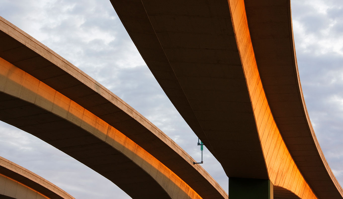 Concrete highway overpass structures photographed from below with golden sunlight against a cloudy sky.