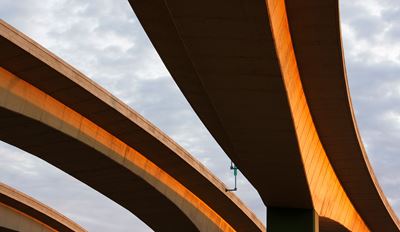 Concrete highway overpass structures photographed from below with golden sunlight against a cloudy sky.