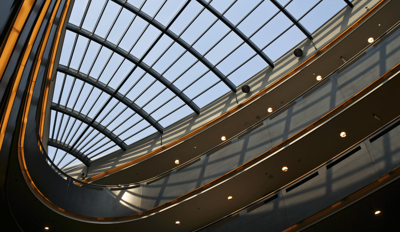 Upward view of a modern building's glass skylight atrium with curved architectural details and ambient lighting