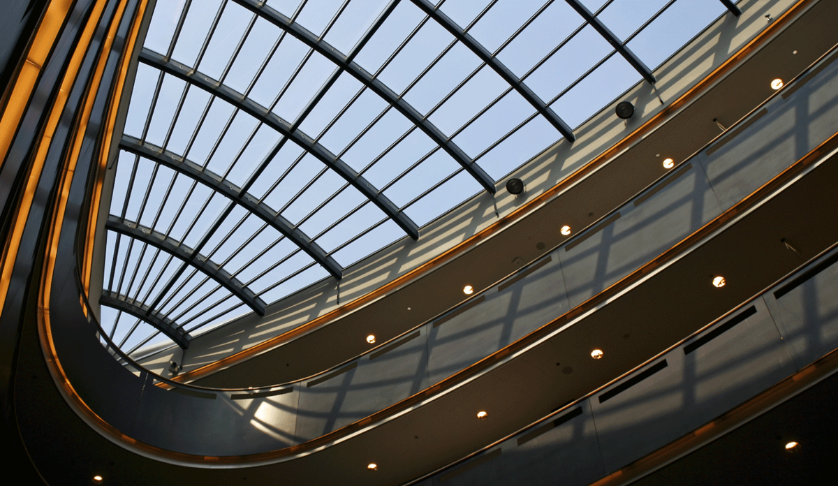 Upward view of a modern building's glass skylight atrium with curved architectural details and ambient lighting