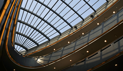 Upward view of a modern building's glass skylight atrium with curved architectural details and ambient lighting