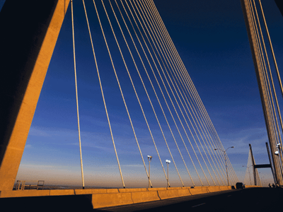 Close-up view of a cable-stayed suspension bridge at sunset, showing the towering support pylon and cables fanning out against a deep blue sky.