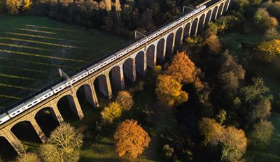 Train on a historic arched viaduct amid fall foliage, aerial view