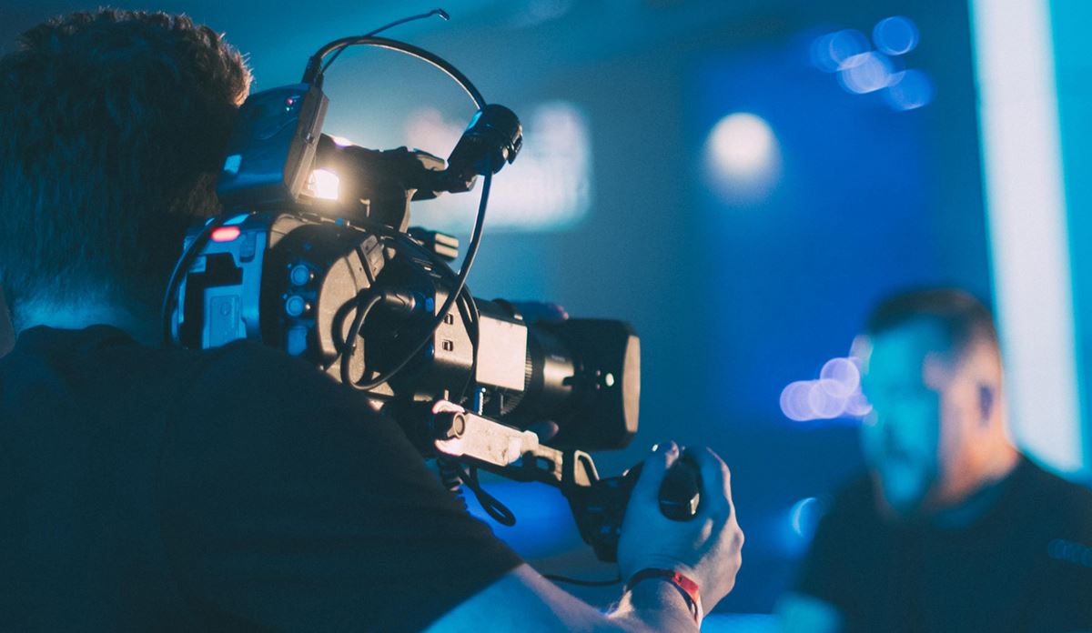 Videographer filming a person in a blue-lit setting.