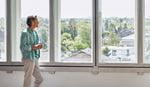 A man stands by a window, gazing thoughtfully outside into the distance.