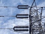 Close-up view of a high-voltage electrical transmission tower with power lines and insulators against a partly cloudy blue sky.