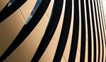 Close-up of a modern building facade featuring curved golden panels with bold dark shadow stripes, creating a dynamic abstract architectural pattern.