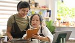 Two women in aprons looking at a tablet together in a modern kitchen