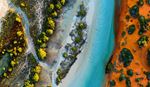 Aerial view of a coastal landscape with turquoise waterways, white sandy shores, green mangrove trees, and vibrant red-orange sand.