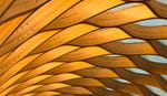 Close-up view of an abstract wooden ceiling structure with interlocking curved beams and visible bolts, illuminated with warm light.
