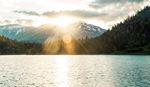 Mountain sunrise over lake with forest and snow-capped peaks