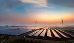 Solar panels and wind turbines at a renewable energy farm during sunrise.