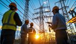 Three men in hard hats stand in front of high voltage power lines, discussing safety measures and project details.