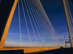 Close-up view of a cable-stayed suspension bridge at sunset, showing the towering support pylon and cables fanning out against a deep blue sky.