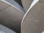 Abstract upward view of curved concrete ramps and metal railings in a multi-level parking structure.