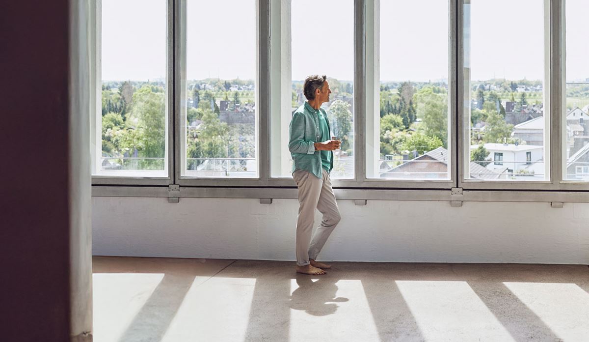 A woman stands alone in a spacious, empty room with expansive windows, creating a bright and airy atmosphere.
