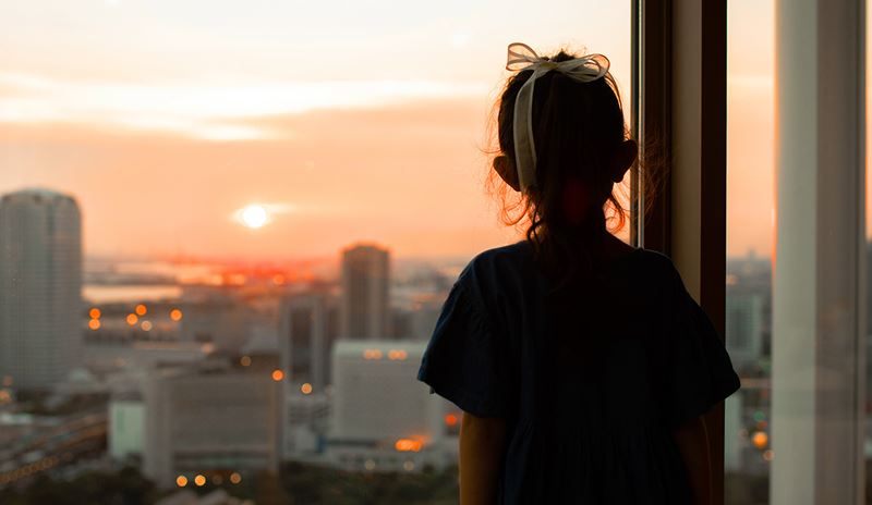 A girl gazes out a window, admiring the vibrant colors of the sunset.