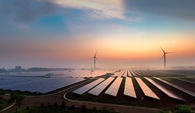 Solar panels and wind turbines at a renewable energy farm during sunrise.