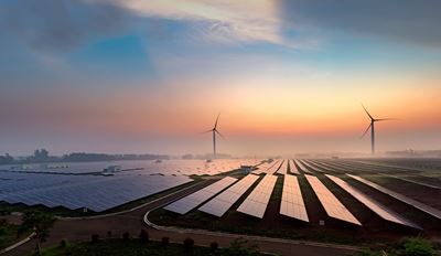 Expansive solar panel field and two wind turbines under a colorful sunrise sky, symbolizing clean energy and sustainability in a serene landscape.