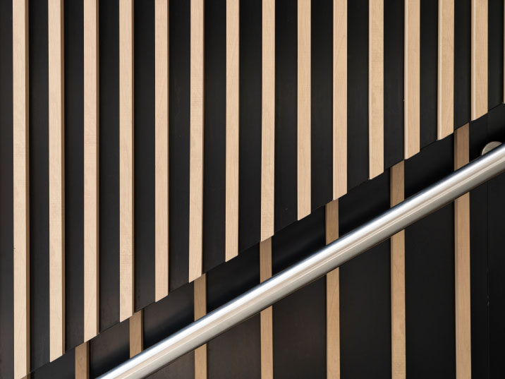 Metal handrail against a striped wood-slat wall.