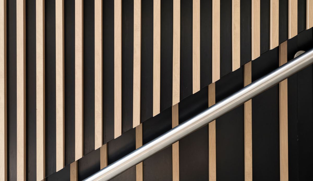 Modern staircase railing against a geometric wood and black slatted wall.