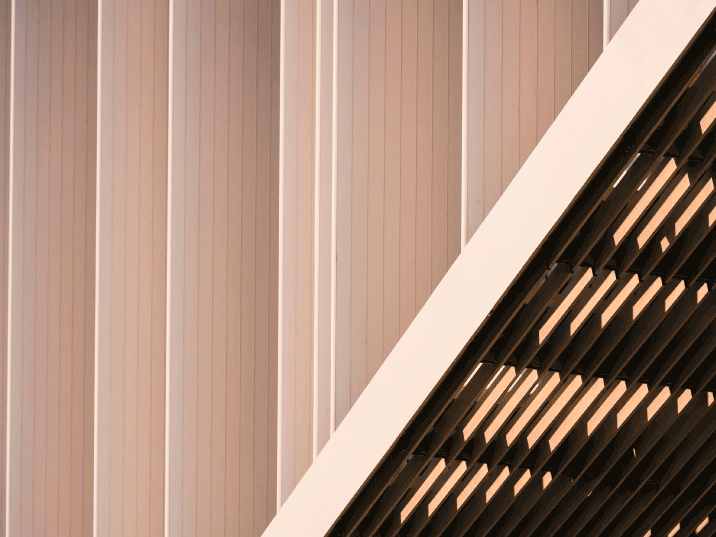 Close-up of a modern building facade with vertical fluted panels and a diagonal louvered roofline.