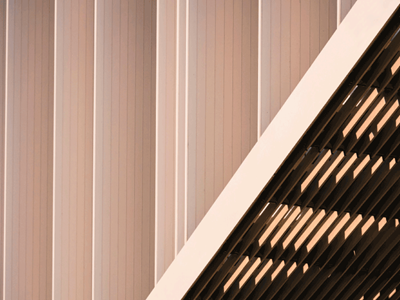 Close-up of a modern building facade with vertical fluted panels and a diagonal louvered roofline.