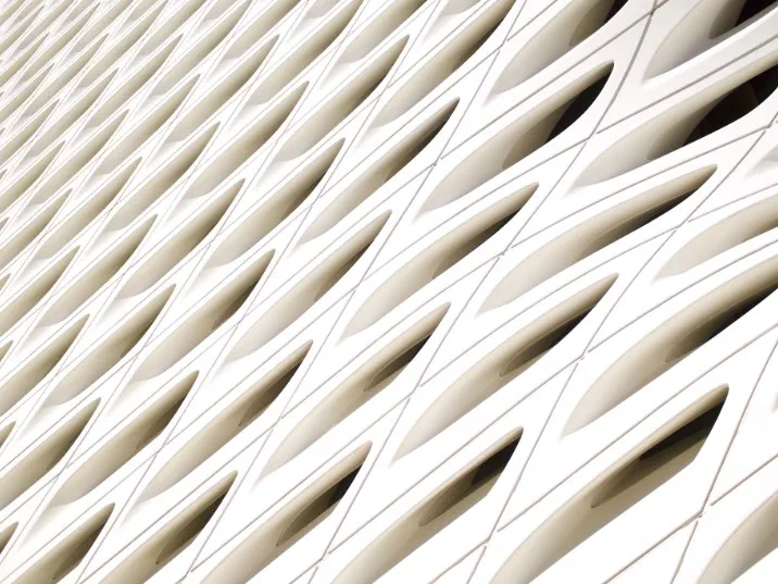 Close-up view of a modern white architectural facade with a repeating pattern of curved, eye-shaped openings arranged in diagonal row.