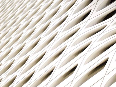 Close-up view of a modern white architectural facade with a repeating pattern of curved, eye-shaped openings arranged in diagonal row.