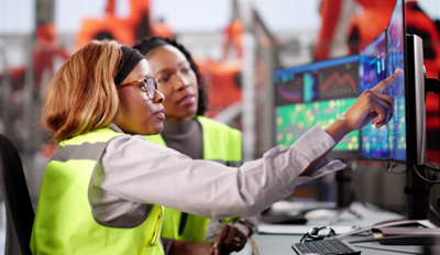 Two manufacturing professionals collaborate at a workstation, analyzing data on monitors in a modern industrial facility.