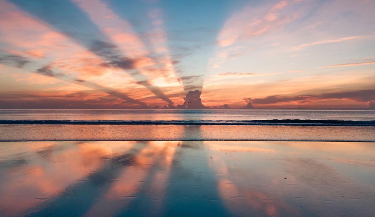 Sunset over a clam ocean with dramatic sun rays reflecting on wet send.