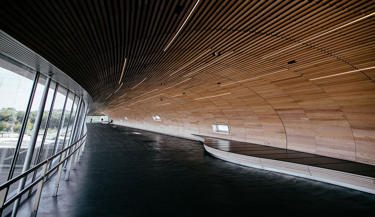 Interior of a modern public infrastructure building featuring curved wooden ceiling panels and floor-to-ceiling glass walls