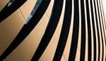 Close-up of a modern building facade featuring curved golden panels with bold dark shadow stripes, creating a dynamic abstract architectural pattern.