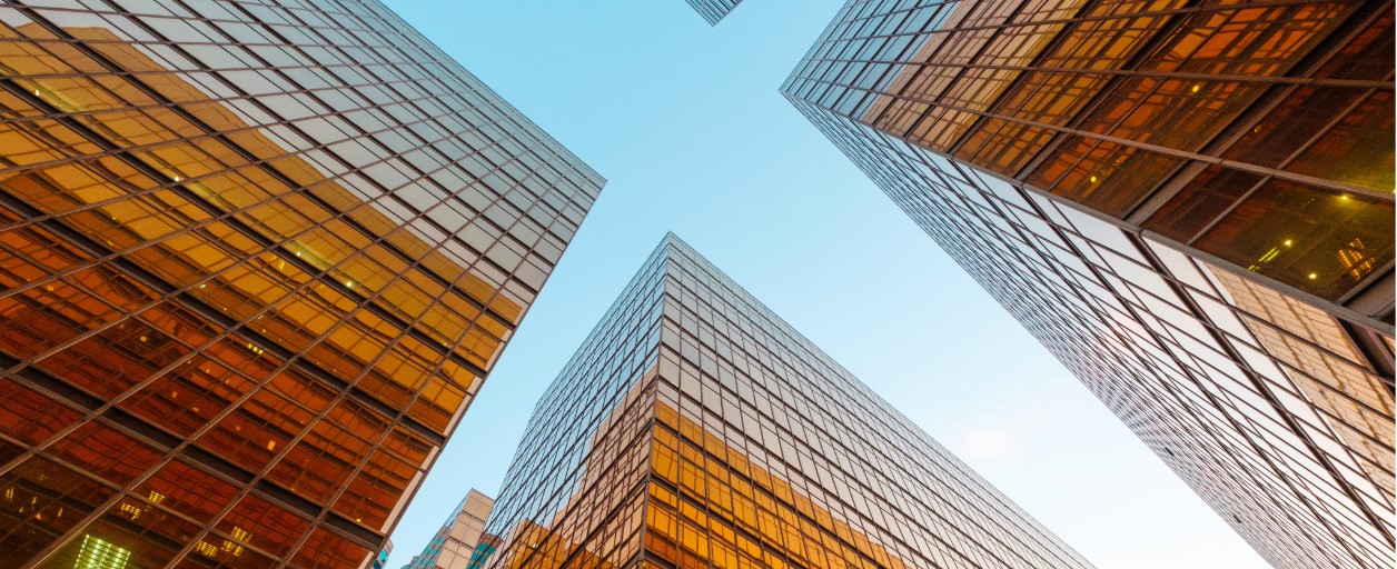 Upward view of glass office towers with golden-toned reflective facades converging against a clear blue sky